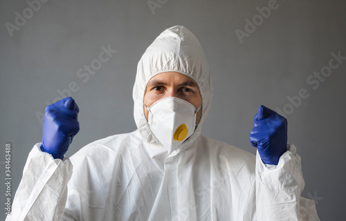 Doctor in white protective suit, medical mask and rubber gloves is showing Fig sign to the virus. Helping a people while coronavirus pandemic threat. Epidemic, pandemic of coronavirus covid 19. photo