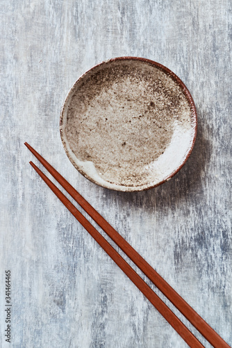 Wooden chopsticks and empty ceramics plate on rustic wooden background. Top view. Copy space.	