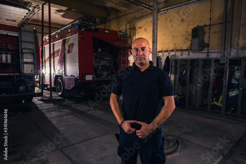 Portrait of handsome firefighter standing against trucks at fire station