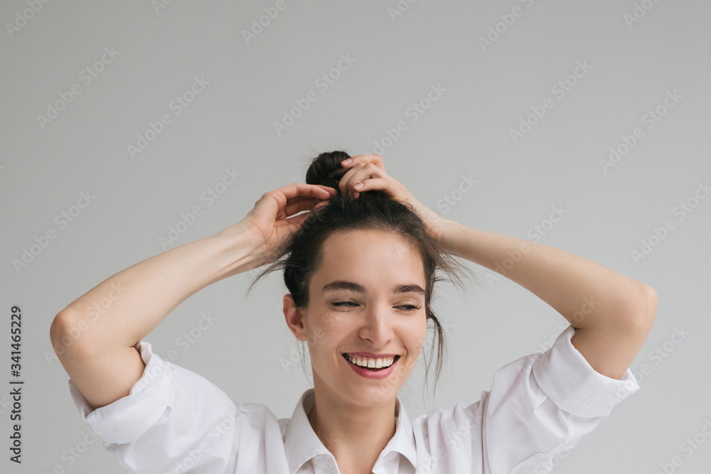 Beautiful caucasian Girl Model Brunette in a white shirt poses, braids her hair. Beautiful smile, unusual beauty, no makeup. Space for text Beautiful caucasian Girl Model Brunette in a white shirt poses, braids her hair. Beautiful smile, unusual beauty, no makeup. Space for text