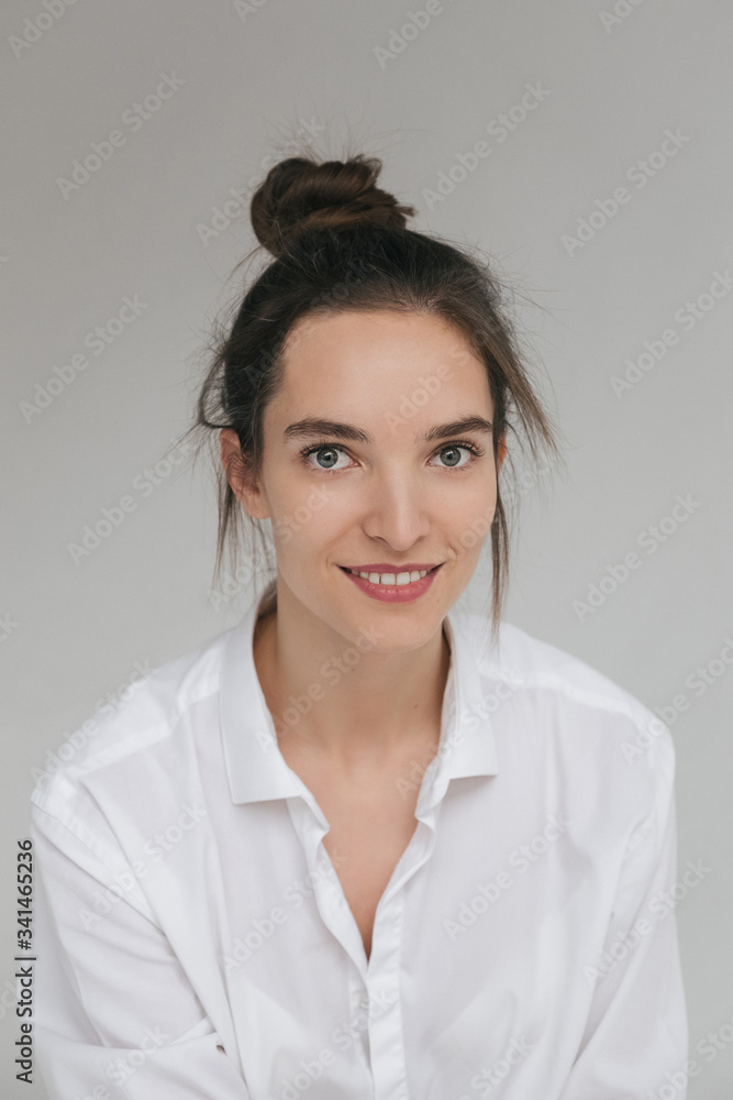 Beautiful caucasian Girl Model Brunette in a white shirt poses, braids her hair. Beautiful smile, unusual beauty, no makeup. Space for text Beautiful caucasian Girl Model Brunette in a white shirt poses, braids her hair. Beautiful smile, unusual beauty, no makeup. Space for text