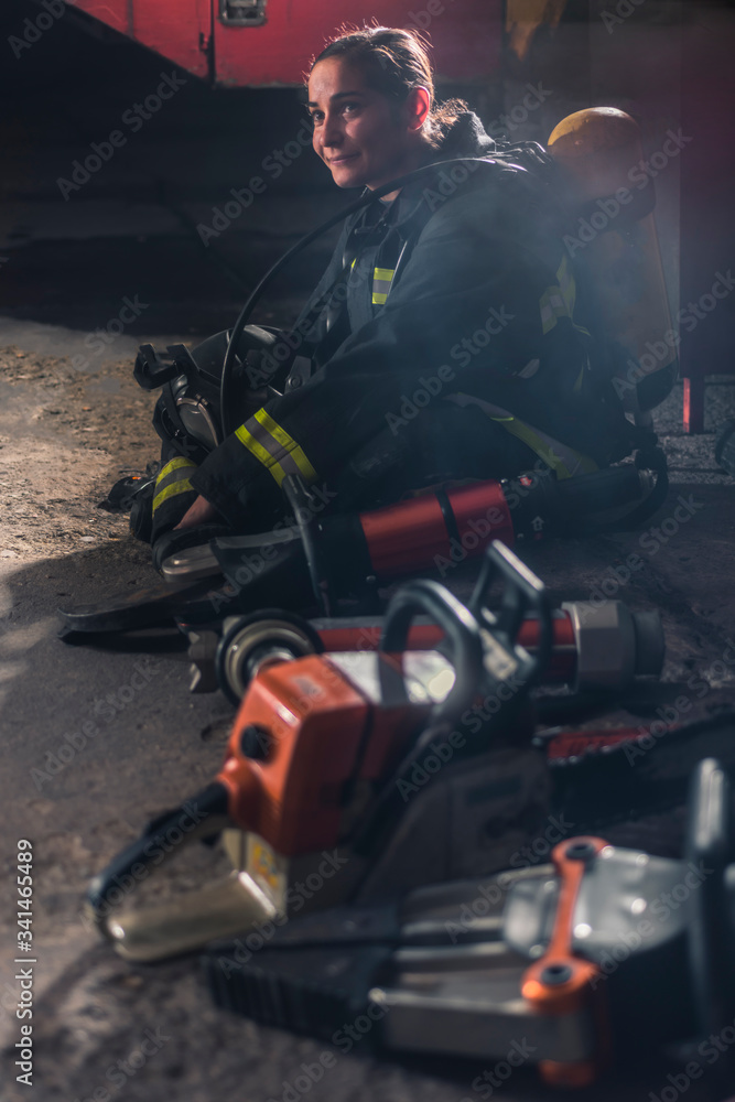 Happy female firefigher sitting content next to her firefighting equipment.