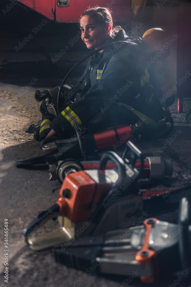 Happy female firefigher sitting content next to her firefighting equipment. Happy female firefigher sitting content next to her firefighting equipment.