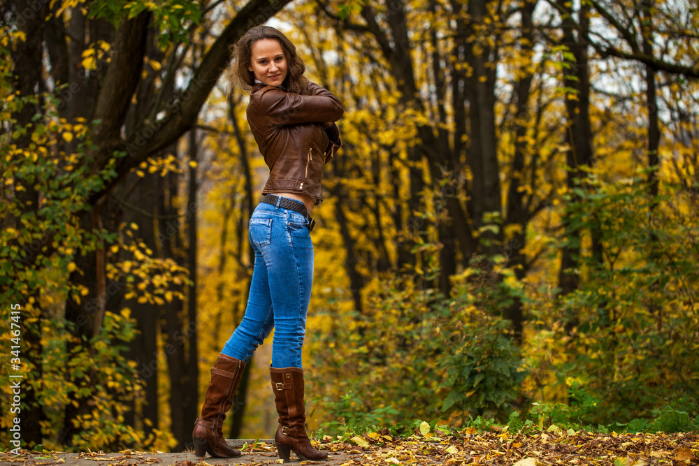 Full body portrait of a young beautiful woman in blue jeans in autumn park