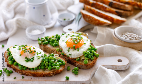 Sourdough bread sandwich with fried egg and stewed green peas on a white table, top view