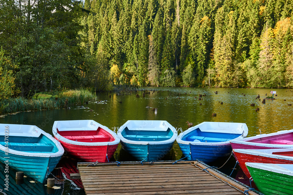 Multi-colored boats at the pier on Lake Lacu Rosu, Romania. Autumn landscape of mountain lake, forest and mountains.