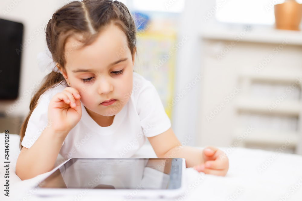 Curious little child girl having fun using digital tablet alone sitting on floor, happy preschool smart kid playing with computer looking at screen watching cartoons online at home Curious little child girl having fun using digital tablet alone sitting on floor, happy preschool smart kid playing with computer looking at screen watching cartoons online at home