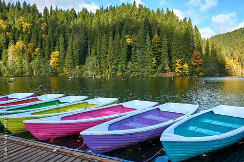 Fototapeta Naklejka Na Ścianę i Meble -  Multi-colored boats at the pier on Lake Lacu Rosu, Romania. Autumn landscape of mountain lake, forest and mountains.