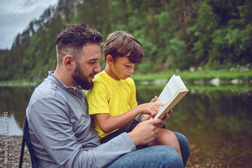 On a hike, on the river bank, father and son read a book