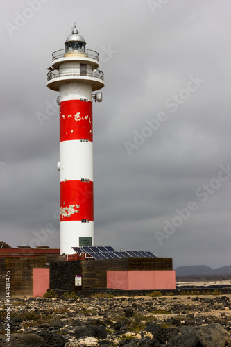 Toston lighthouse with red and white bands on cloudy day in Fuerteventura. Tall beacon with worn out paint. Unattended, abandoned concepts