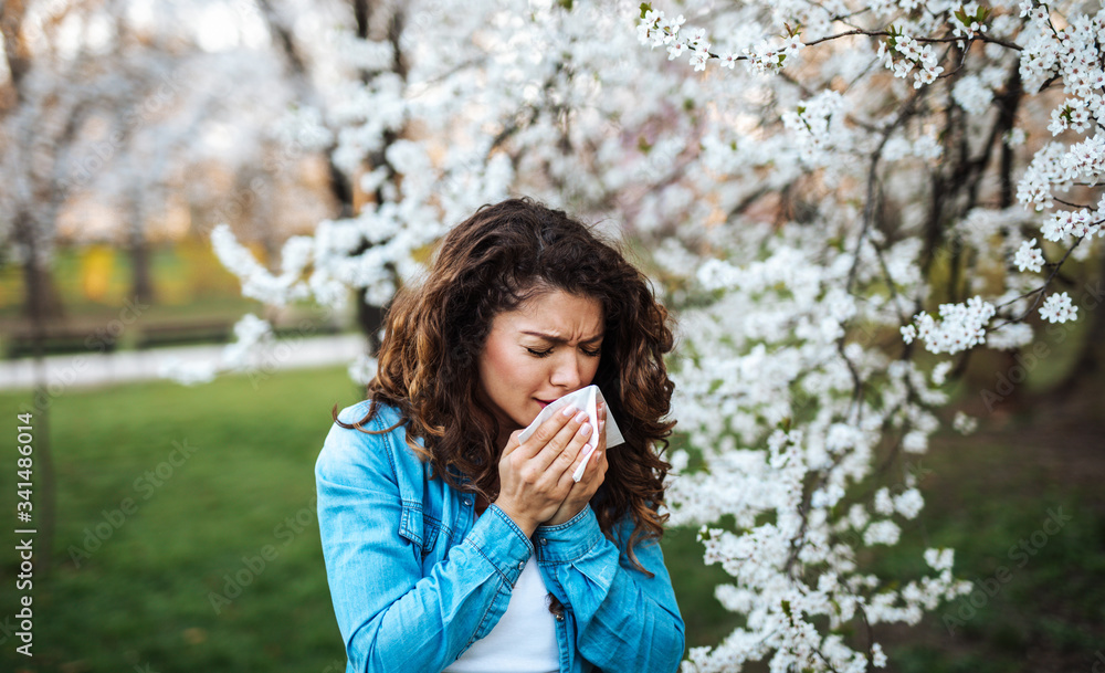 Young woman sneezing in park. Allergy, flu, virus concept Young woman sneezing in park. Allergy, flu, virus concept
