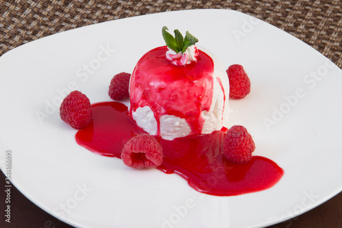 Whipped cream in raspberry syrup and with raspberries on a large white plate on a brown background