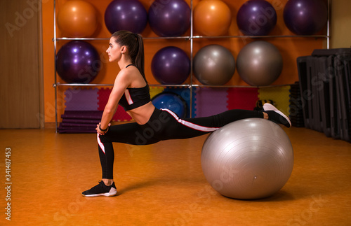 Young sportswoman doing exercises with swiss ball in fitness club