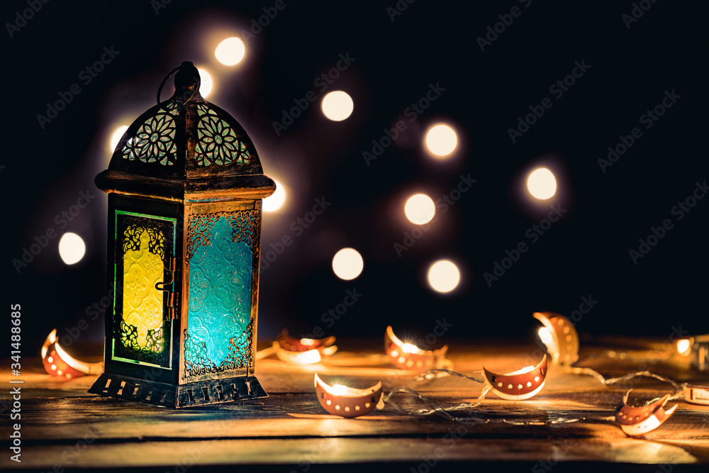Ramadan Lantern with Colorful Light Glowing at Night and Glittering with Bokeh Lights on Ground. Festive Greeting Card, Invitation for Muslim Holy Month Ramadan Kareem. Dark background Ramadan Lantern with Colorful Light Glowing at Night and Glittering with Bokeh Lights on Ground. Festive Greeting Card, Invitation for Muslim Holy Month Ramadan Kareem. Dark background