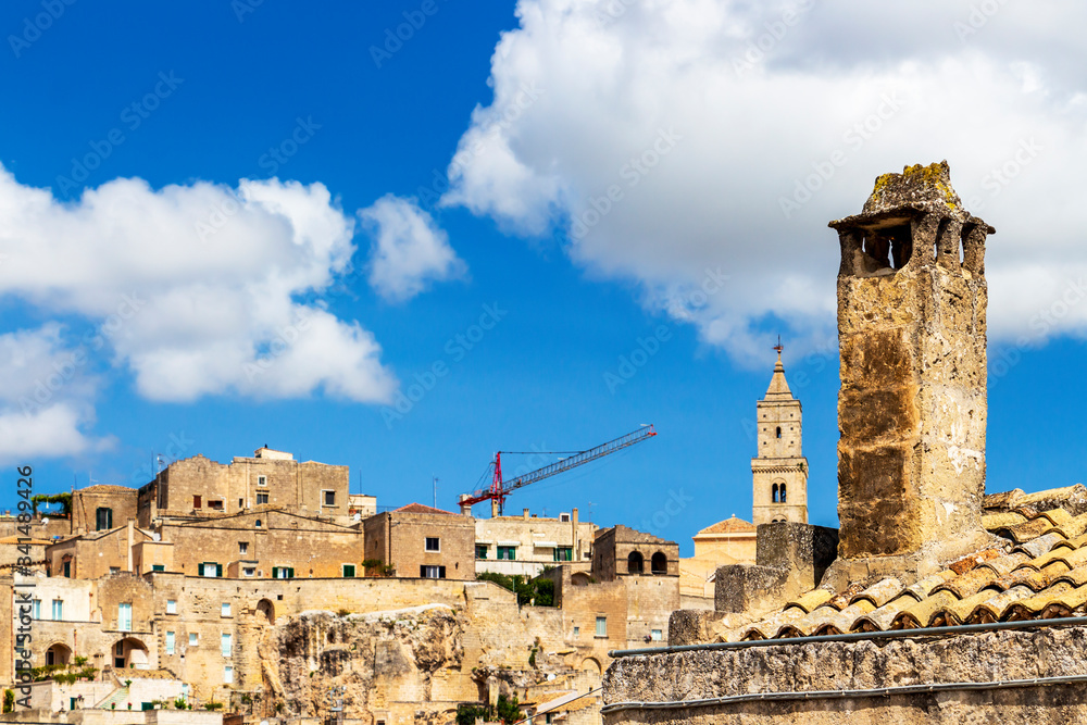 Traditional high chimney in front of blurred Matera old town skyline with a construction crane in Matera, Province of Matera, Basilicata Region, Italy
