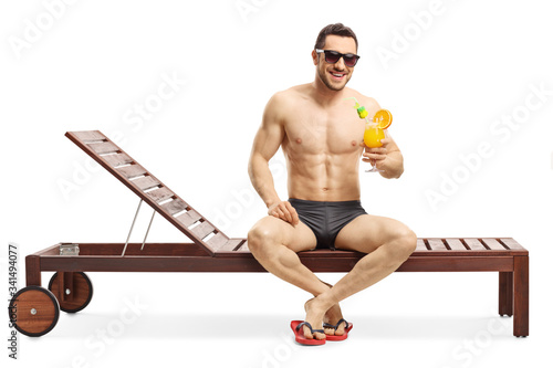 Murais de parede Young attractive man sitting on a sunbed and holding a cocktail