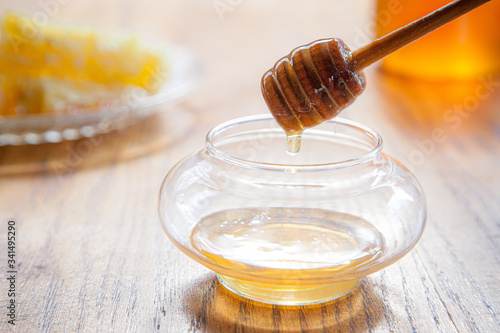 Raw honey dripping off dipper into clear glass bowl on wooden tabletop