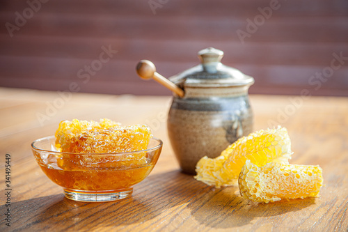 Organic honeycomb in glass bowl with rustic jar on wooden table