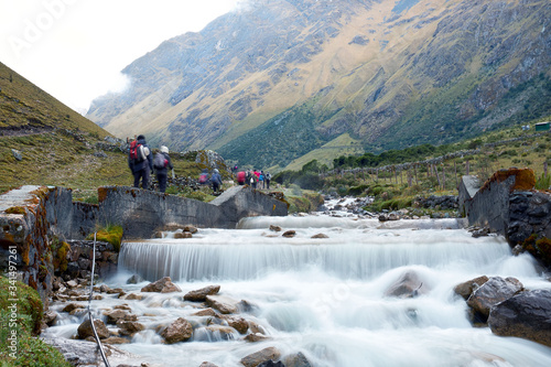 Hikers walk along a river in the Andes photo