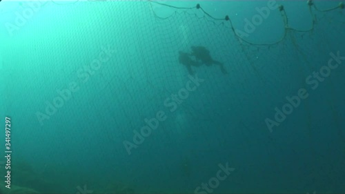 scuba divers around old ghost fhish net underwater dangerous ocean scenery photo