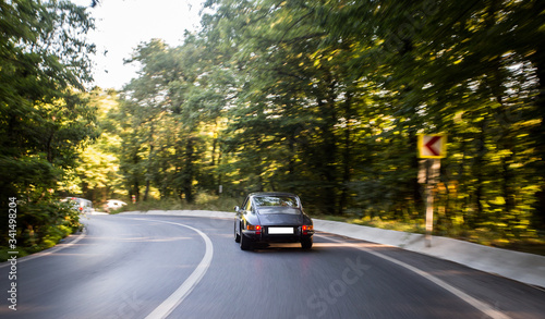 Urban drive with a black sedan car in the sunset across green trees