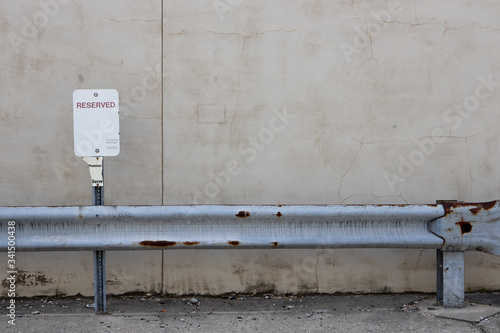 Reserved blank parking sign with metal rusting guard rail in front and stucco wall behind