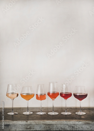 Various shades of Rose wine in stemmed glasses placed in line from light to dark colour, white wall background behind, copy space. Wine bar, wine shop, wine tasting concept