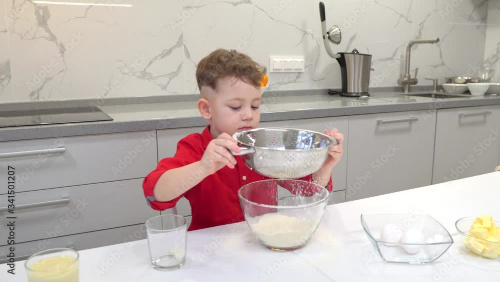 Cute little boy sifting flour over bowl while going to make dough for homemade pastry in the kitchen Cute little boy sifting flour over bowl while going to make dough for homemade pastry in the kitchen