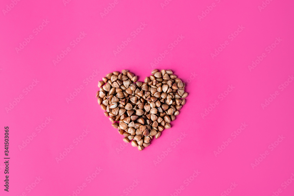 Top view of the heart with uncooked buckwheat isolated on the pink magenta background. gluten free ancient grain for healthy diet, selective focus.