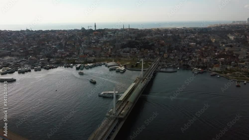 Air view of Golden Horn Metro Bridge on cloudy day, Bosphorus Halic bay.Drone is flying towards the Blue Mosque. European part of the city. Pleasure boat with tourists floating along the bay. Air view of Golden Horn Metro Bridge on cloudy day, Bosphorus Halic bay.Drone is flying towards the Blue Mosque. European part of the city. Pleasure boat with tourists floating along the bay.