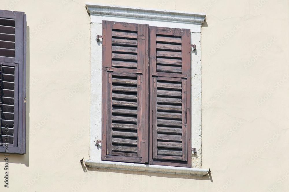 Italian window on the bright wall facade with closed wooden shabby brown color shutters