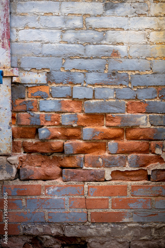 Deteriorated and worn old red brick wall with grey blue paint on some bricks and rusted drain pipe
