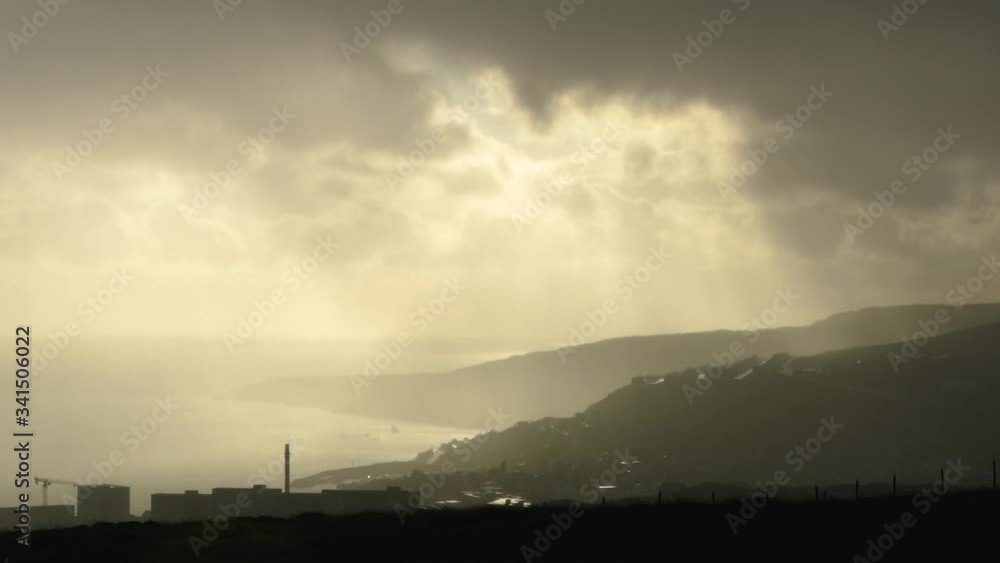 Aerial ray of sun light behind moving clouds and a city near the sea down the mountains Aerial ray of sun light behind moving clouds and a city near the sea down the mountains