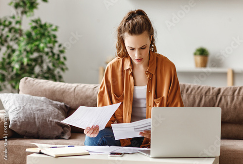 Pensive stressful female employee examining reports while working on complicated project at home.