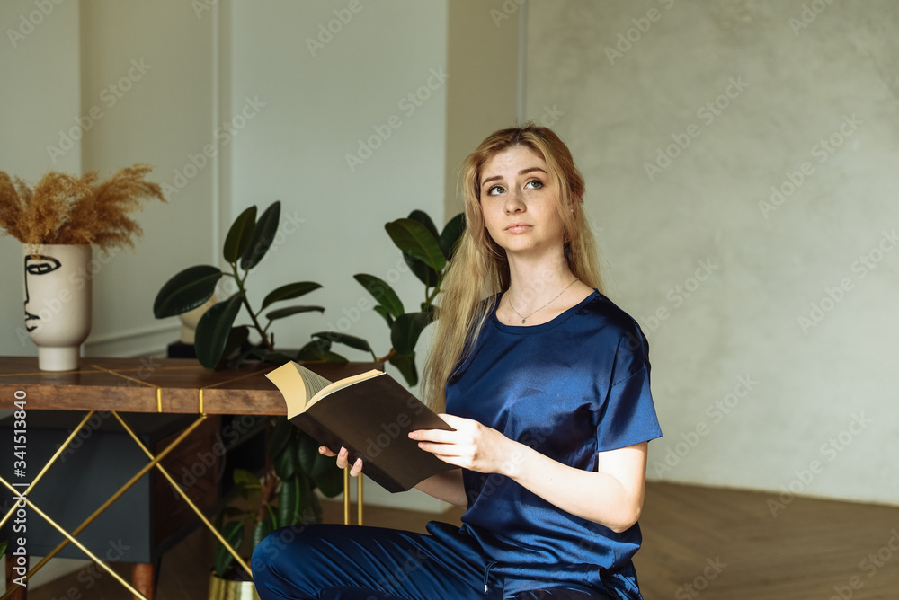 The beautiful blonde thought about the meaning of the book. A young woman is sitting at home and reading a book The beautiful blonde thought about the meaning of the book. A young woman is sitting at home and reading a book