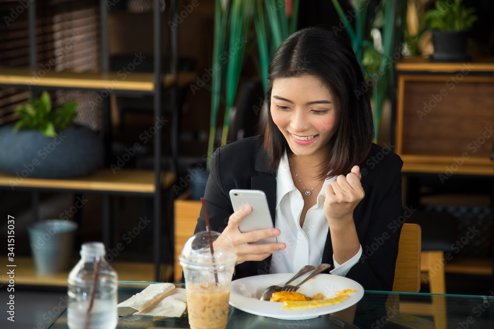 Close up charming young Asian woman in formal wear sitting at coffee shop after lunch, She is smiling receiving good news from the smarth phone.