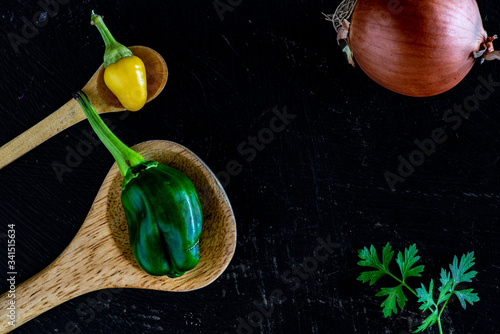 Draufsicht von zwei hölzernen Küchenlöffeln mit Paprika und Jalapeño in einem schwarzen hölzernen Kochtisch photo