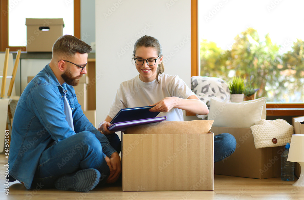 Happy couple looking at photo album while unpacking stuff after relocation to new flat Happy couple looking at photo album while unpacking stuff after relocation to new flat