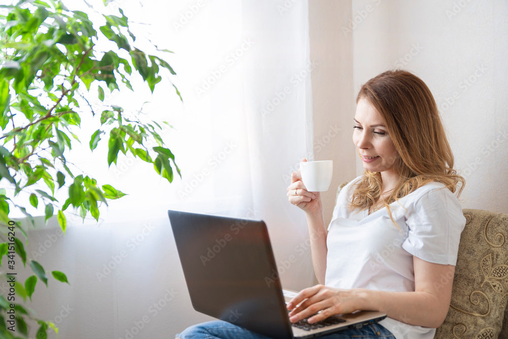 Beautiful young woman working on laptop computer while sitting at the living room, drinking coffee. Beautiful young woman working on laptop computer while sitting at the living room, drinking coffee.