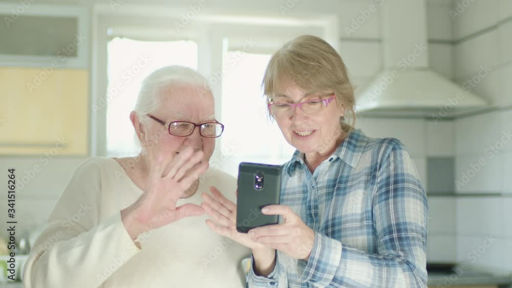 Daughter And Her Old Mom Talking On The Phone With Someone. They Wave Their Hands In Greeting.