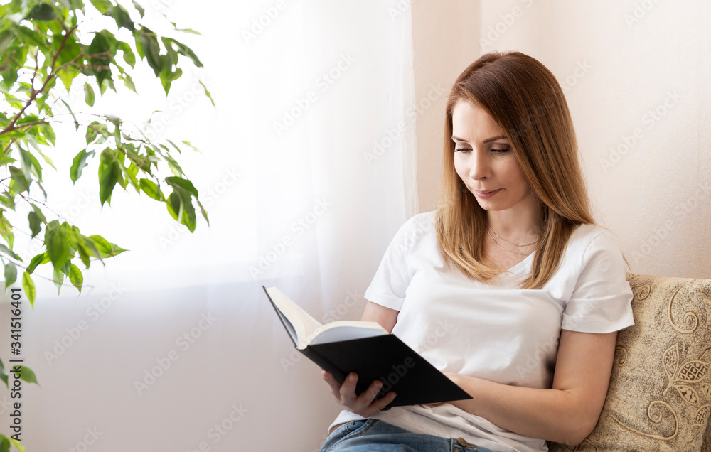 Happy young woman reading storybook on couch at home Happy young woman reading storybook on couch at home