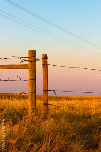 Wooden and Wire Fence posts over a dry grass field with power lines overhead and a rainbow colored sky