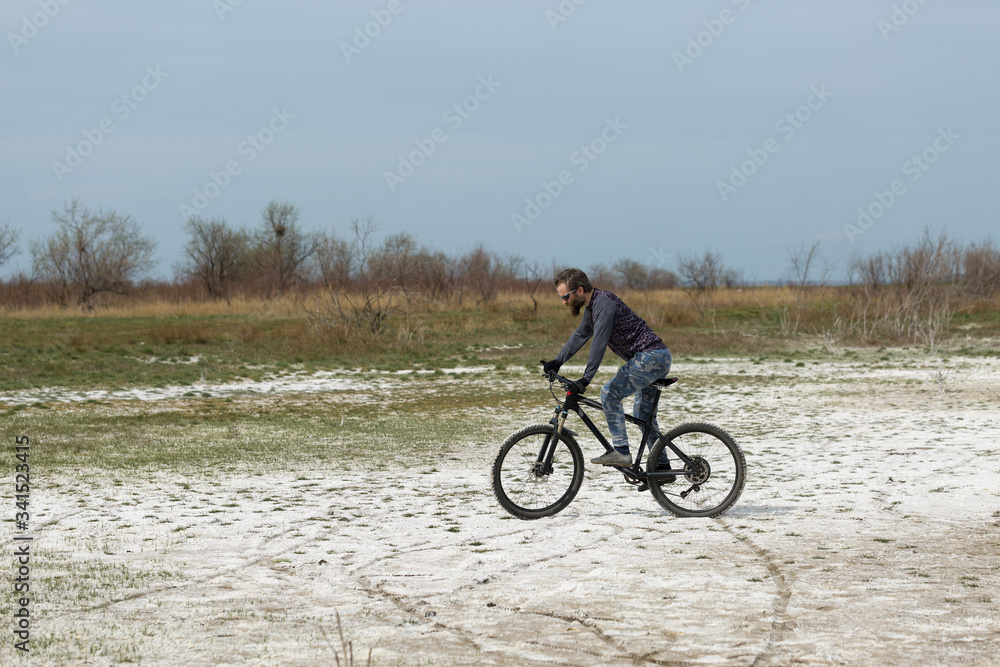 Obraz premium Sports brutal bearded guy on a modern mountain bike. A cyclist in a salt deserted place by the lake.