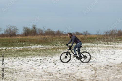 Sports brutal bearded guy on a modern mountain bike. A cyclist in a salt deserted place by the lake.