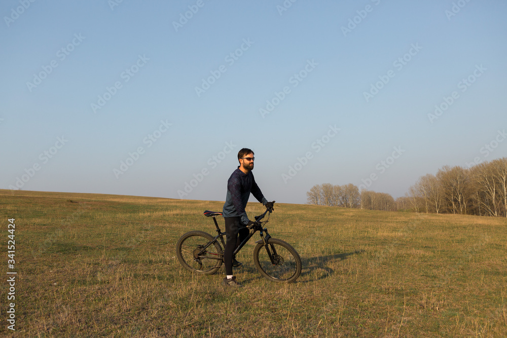 Cyclist in shorts and jersey on a modern carbon hardtail bike with an air suspension fork standing on a cliff against the background of fresh green spring forest Cyclist in shorts and jersey on a modern carbon hardtail bike with an air suspension fork standing on a cliff against the background of fresh green spring forest