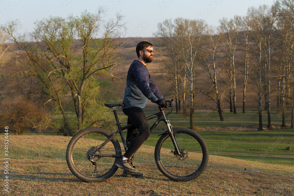 Cyclist in shorts and jersey on a modern carbon hardtail bike with an air suspension fork standing on a cliff against the background of fresh green spring forest