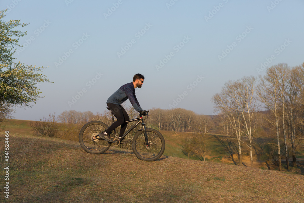 Cyclist in shorts and jersey on a modern carbon hardtail bike with an air suspension fork standing on a cliff against the background of fresh green spring forest