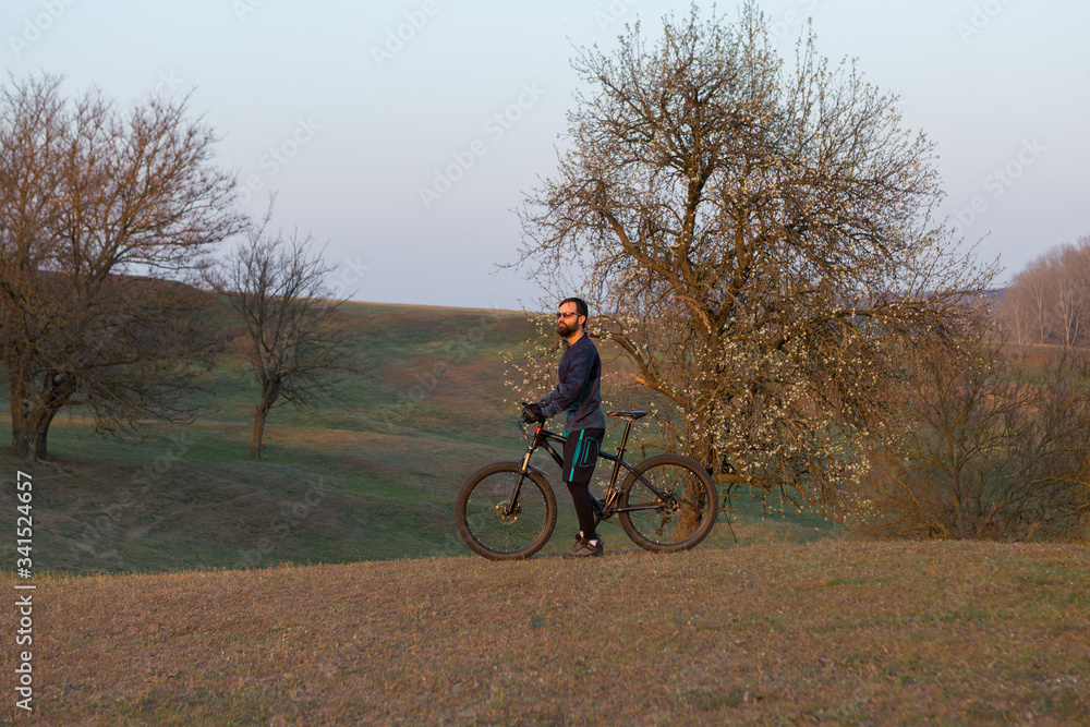 Cyclist in shorts and jersey on a modern carbon hardtail bike with an air suspension fork standing on a cliff against the background of fresh green spring forest Cyclist in shorts and jersey on a modern carbon hardtail bike with an air suspension fork standing on a cliff against the background of fresh green spring forest