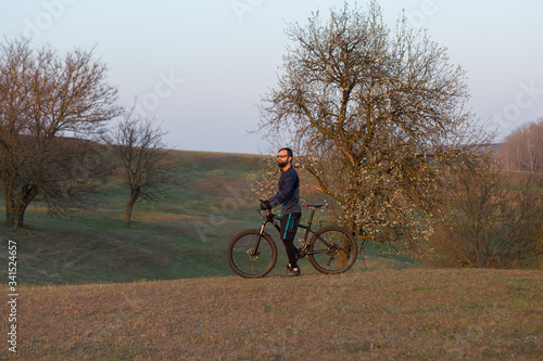 Cyclist in shorts and jersey on a modern carbon hardtail bike with an air suspension fork standing on a cliff against the background of fresh green spring forest