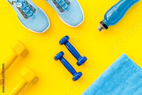 Athletics flat-lay with dumbbells, towel, sneakers on yellow background top-down